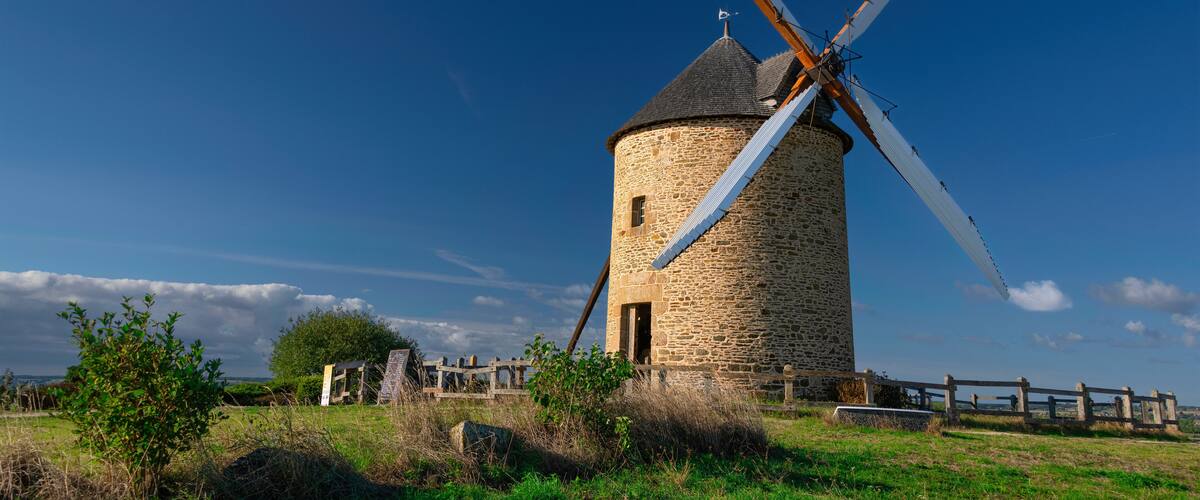 A stone windmill with a wooden fence in a grassy field.
