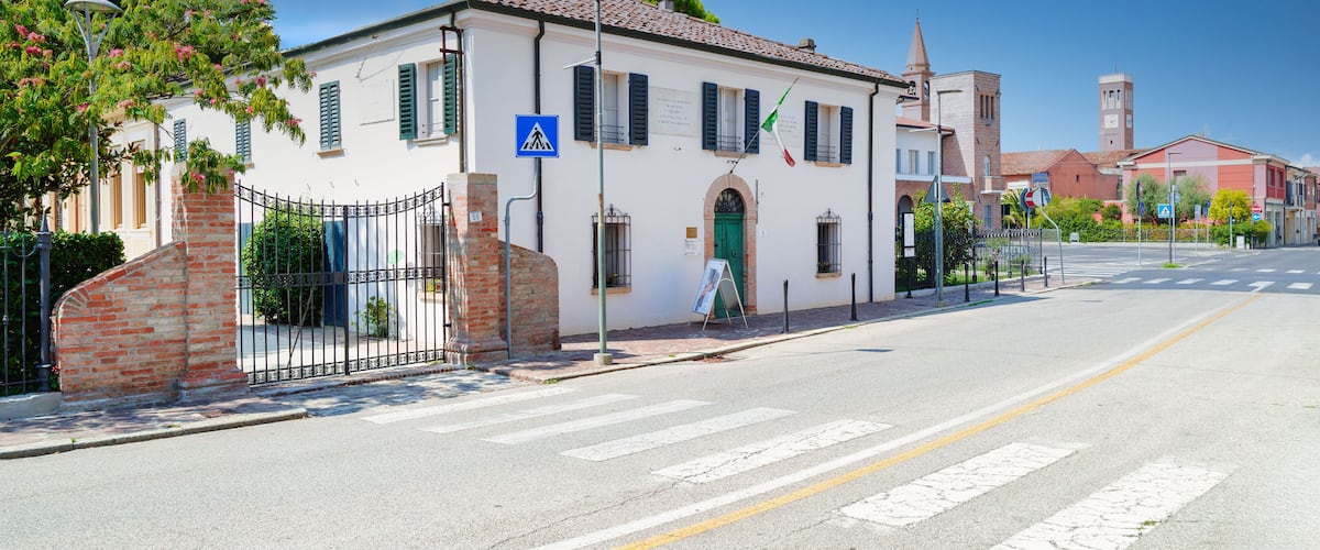 A white building with green shutters, a brick gate, and a clear blue sky.