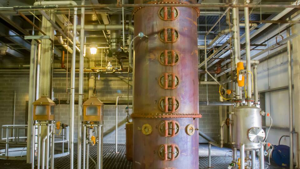 A large industrial structure with multiple valves and pipes, surrounded by metal scaffolding and a brick wall.