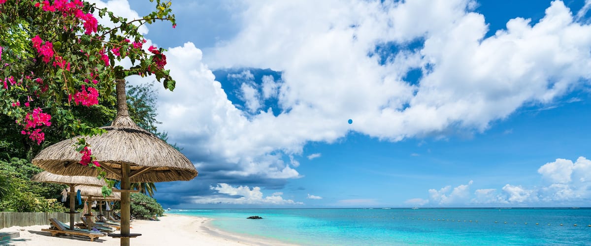 A beach with white sand, clear turquoise water, and a thatched umbrella.