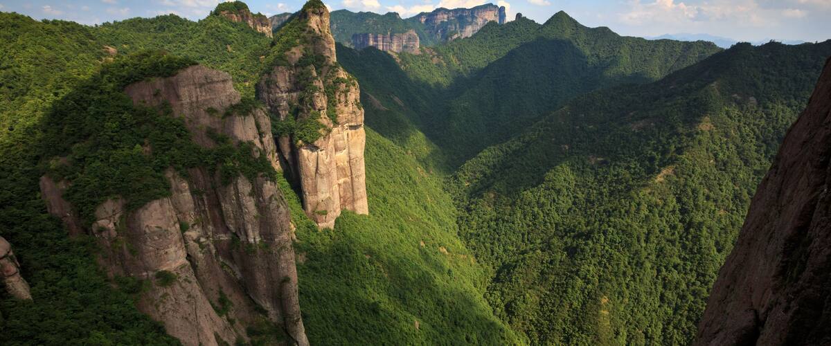 A mountainous landscape with a prominent rock formation and dense forest.