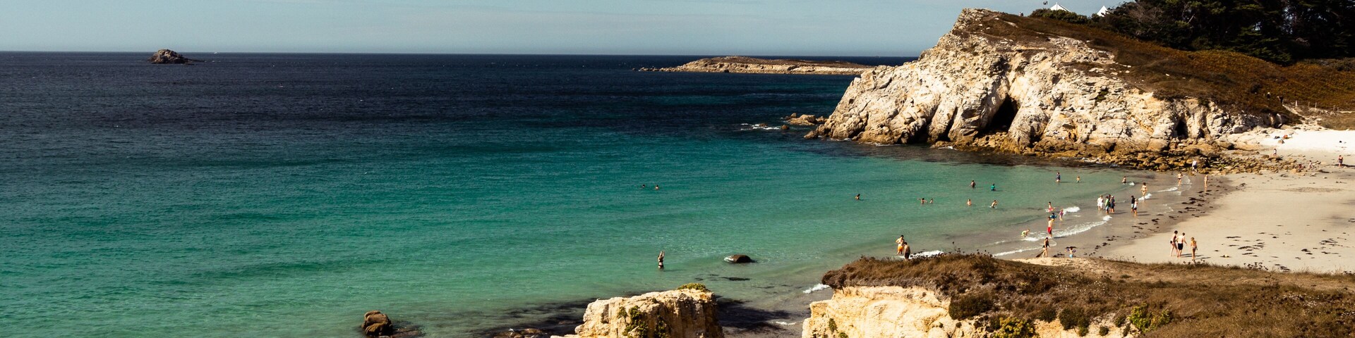 Paisagem costeira com águas turquesa cristalinas, falésias rochosas e uma praia arenosa.
