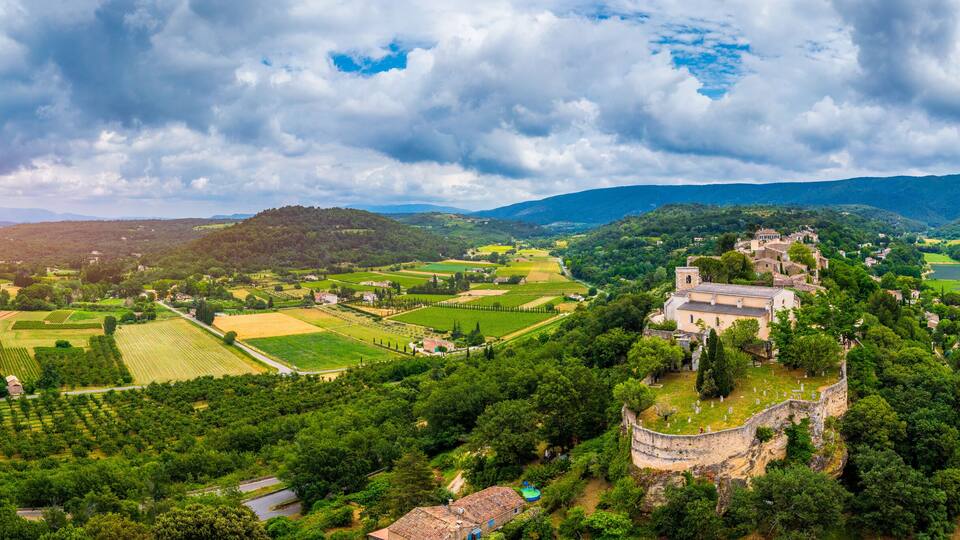 A lush valley with vineyards, a historic church, and rolling hills under a cloudy sky.