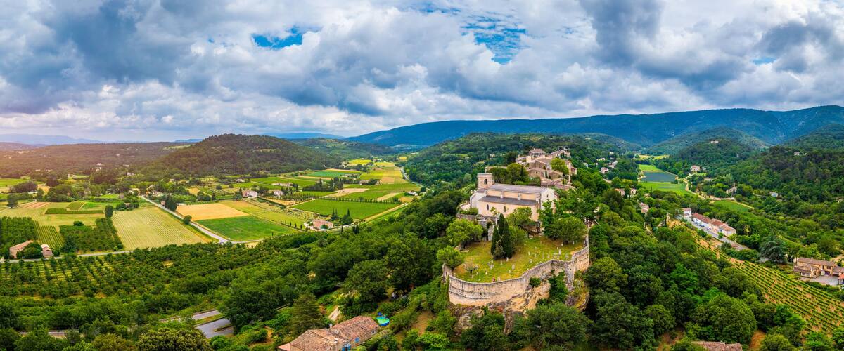 A lush valley with vineyards, a historic church, and rolling hills under a cloudy sky.