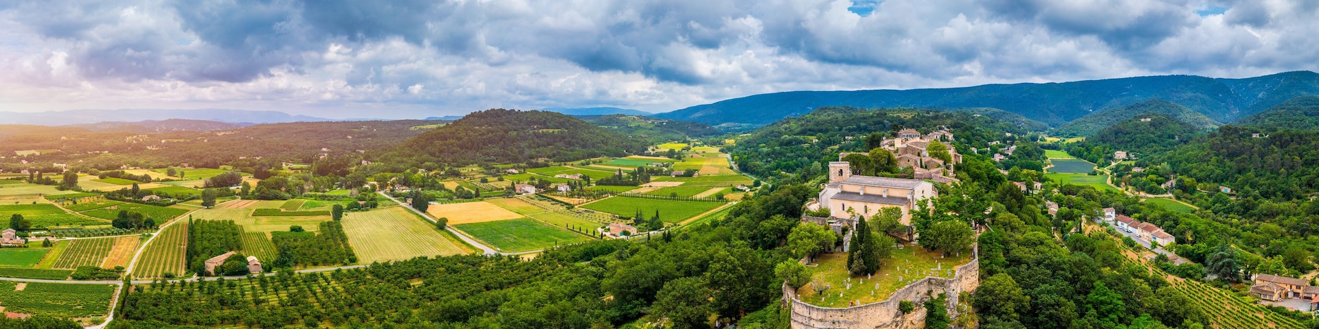 A lush valley with vineyards, a historic church, and rolling hills under a cloudy sky.