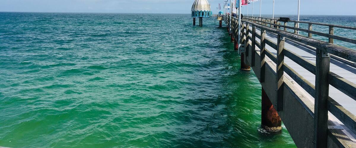 A pier extending into the ocean with flags and a domed structure in the distance.
