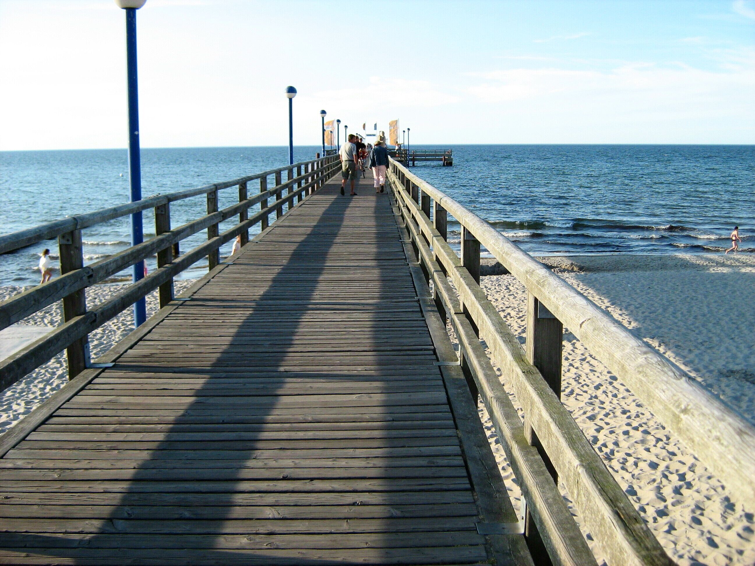 A wooden pier extending into the ocean with people walking along it.