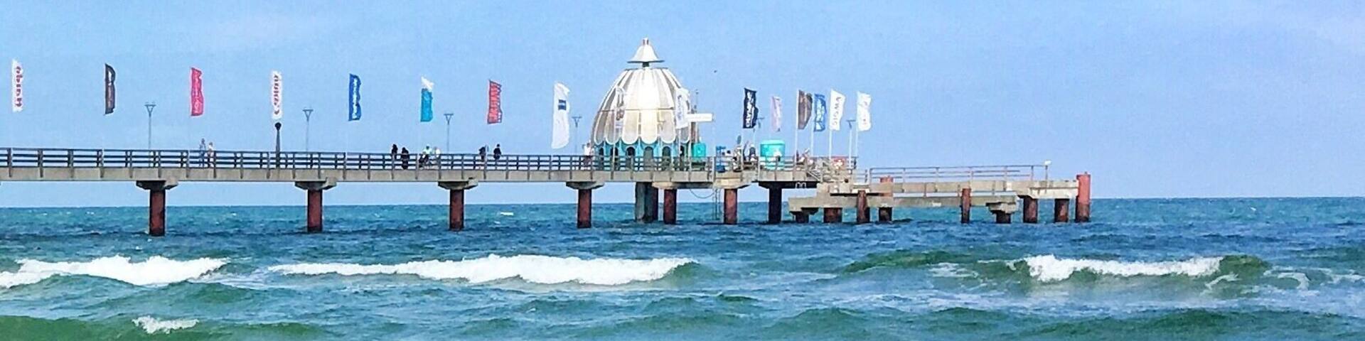 A pier extending into the ocean with a white dome structure in the center, surrounded by flags.