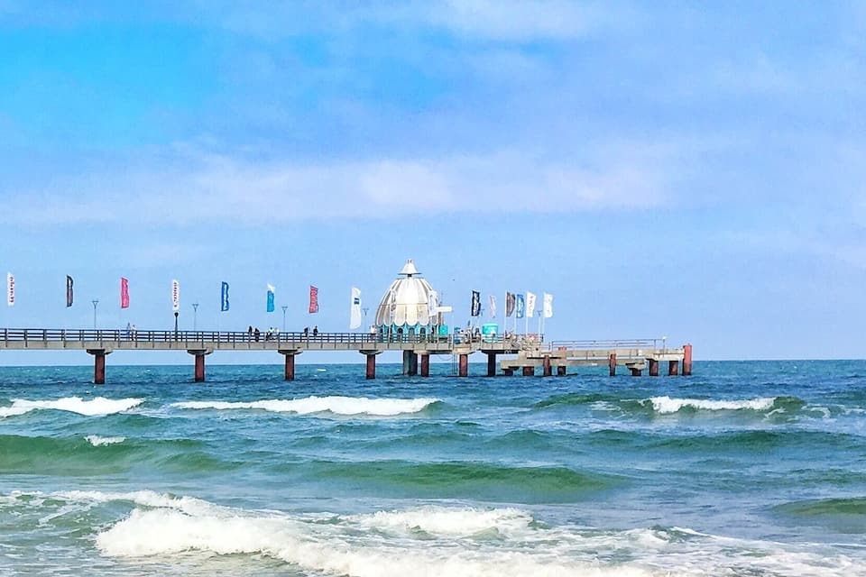 Une jetée s’avançant dans l’océan, surmontée d’une structure en forme de dôme blanc au centre, et entourée de drapeaux.