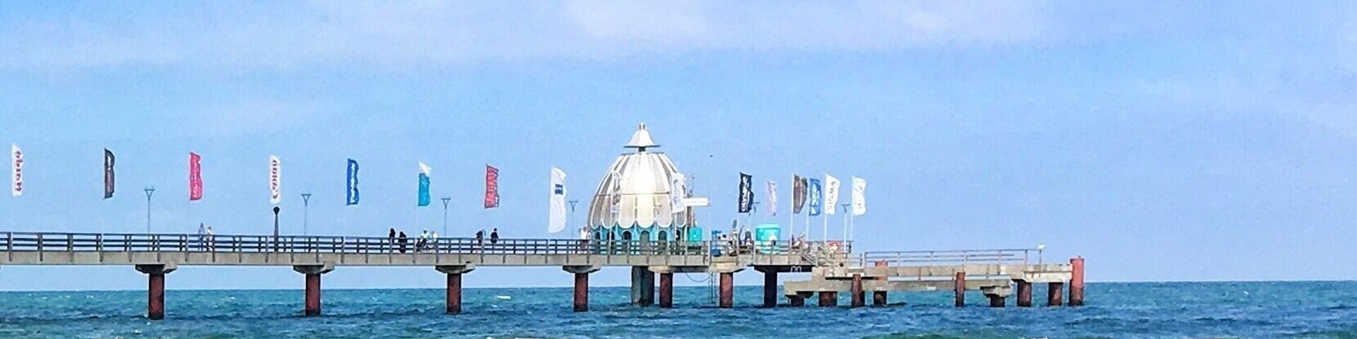 En moler, der strækker sig ud i havet, med en hvid kuppelstruktur i midten, omgivet af flag.