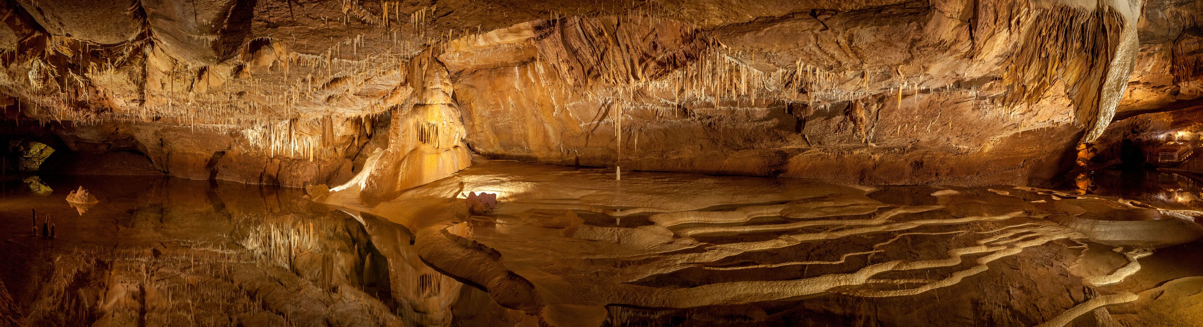 A cave with stalactites and a reflective water pool.