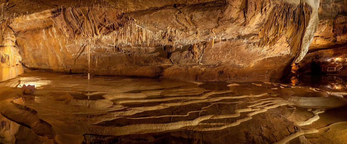 A cave with stalactites and a reflective water pool.