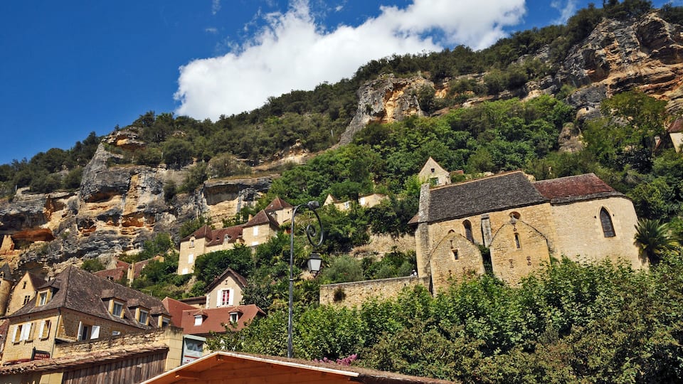A hillside village with stone buildings, lush greenery, and a prominent church.