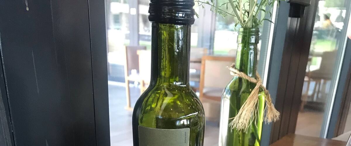 A bottle of Finca 1883 olive oil, a piece of bread, and a small bowl of olive oil on a wooden table.