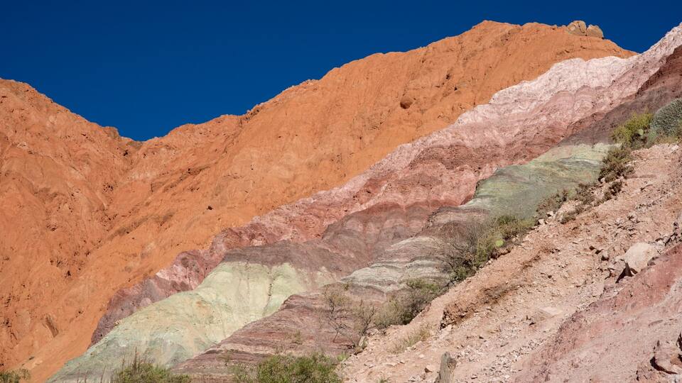 A layered rock formation with distinct strata of red, pink, and green colors.