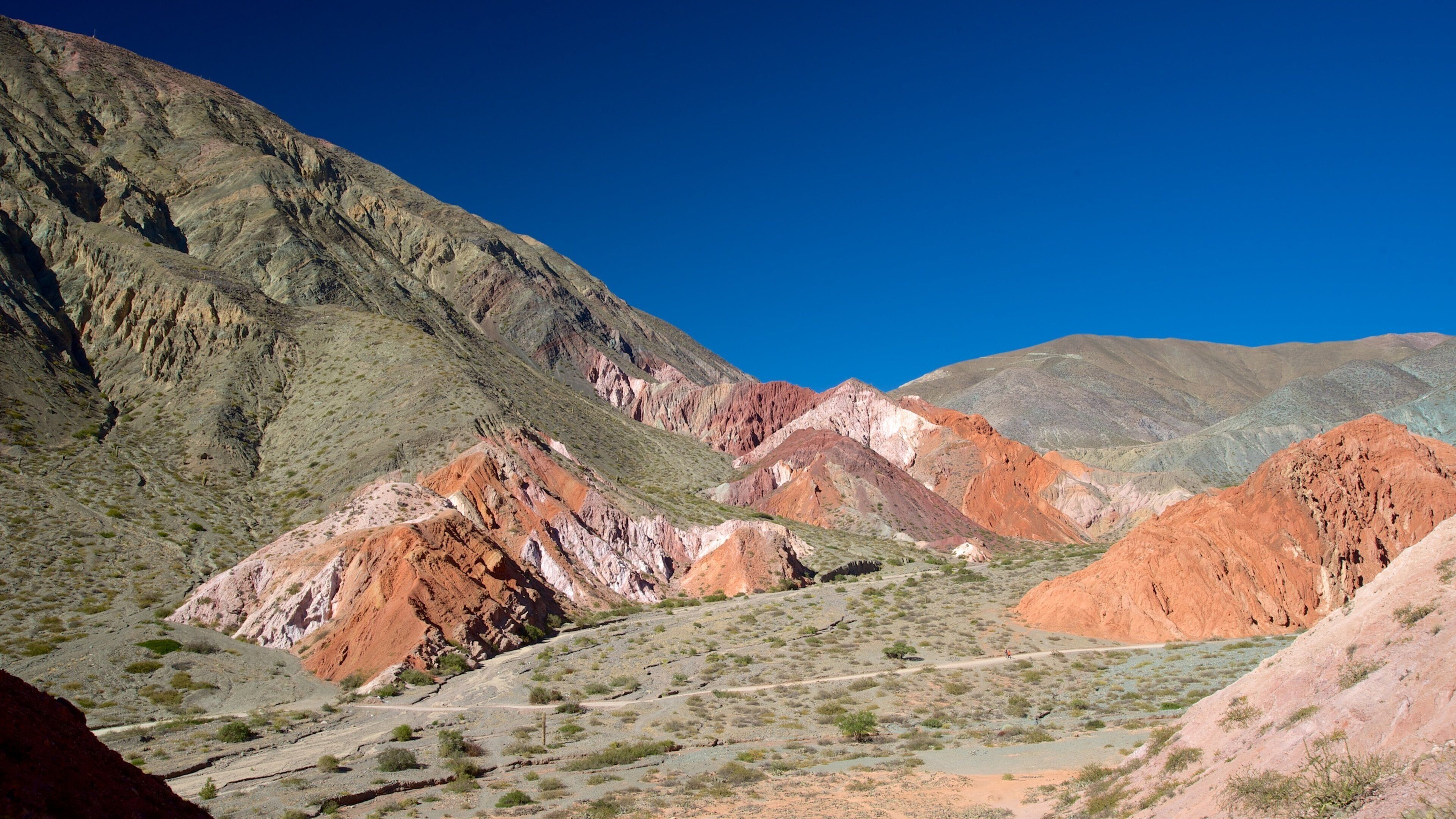 A rugged mountain landscape with red and green rock formations under a clear blue sky.