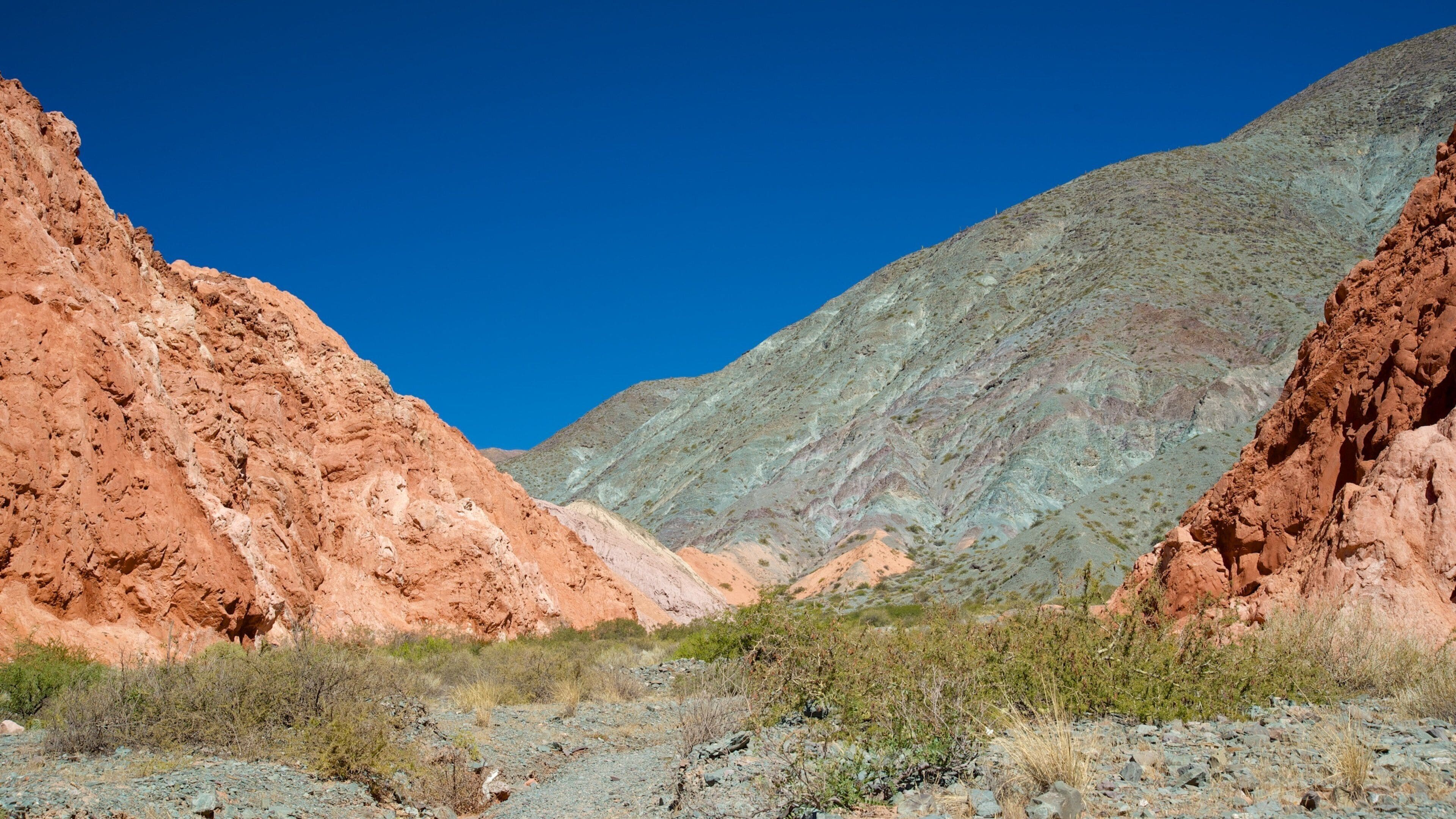 A rugged mountain landscape with reddish-brown cliffs and a clear blue sky.
