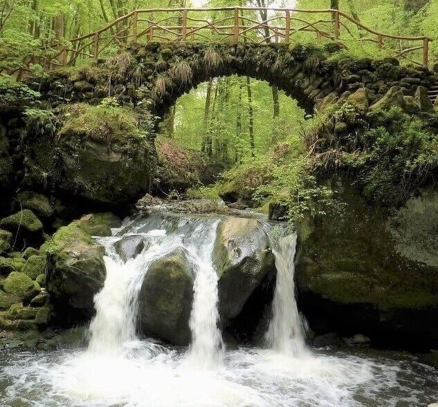 A stone bridge over a waterfall in a forest.