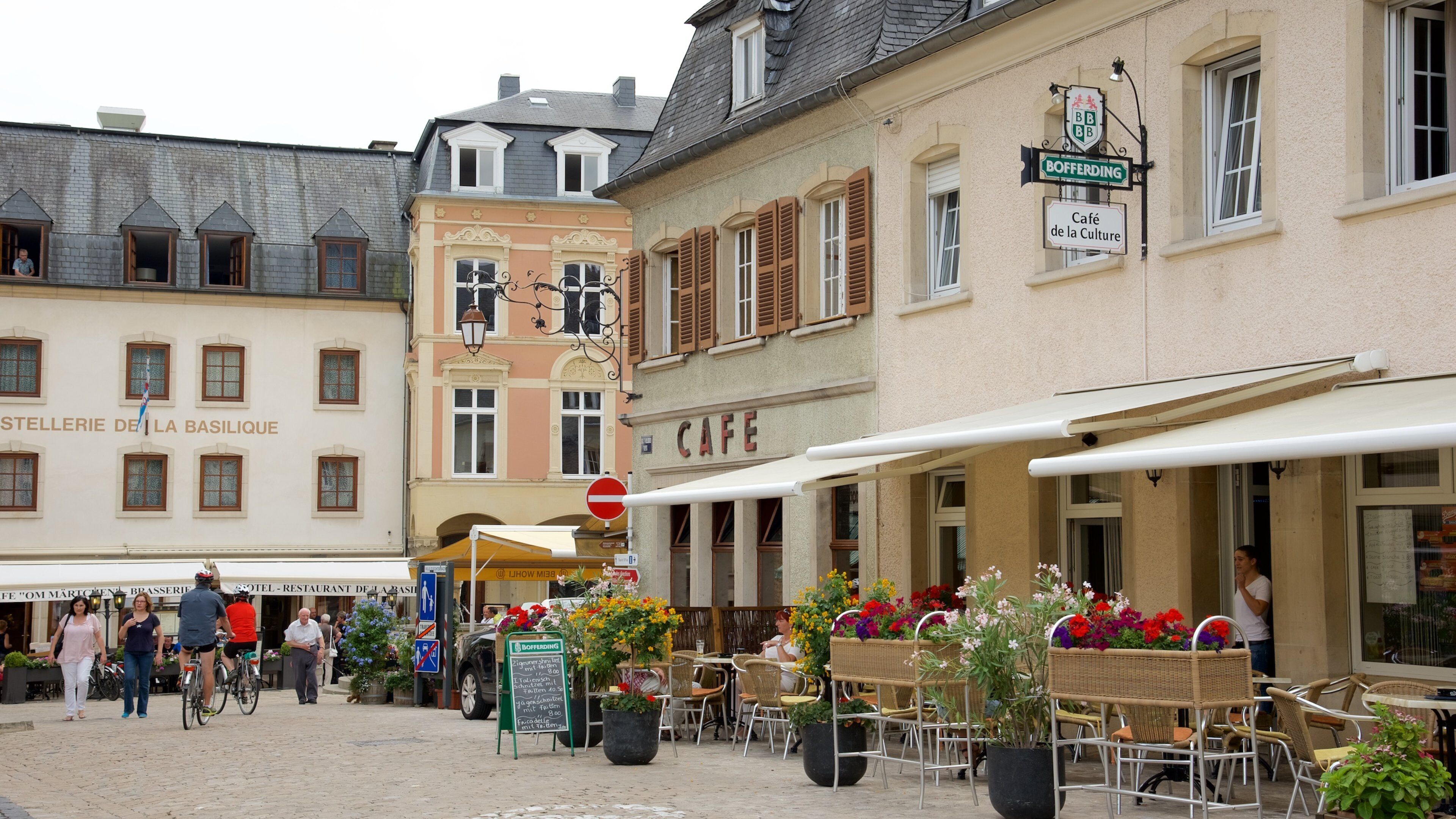 A street with cafes, outdoor seating, and flower baskets.
