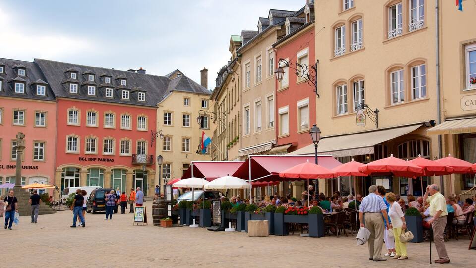 A bustling outdoor market with red umbrellas and people shopping.