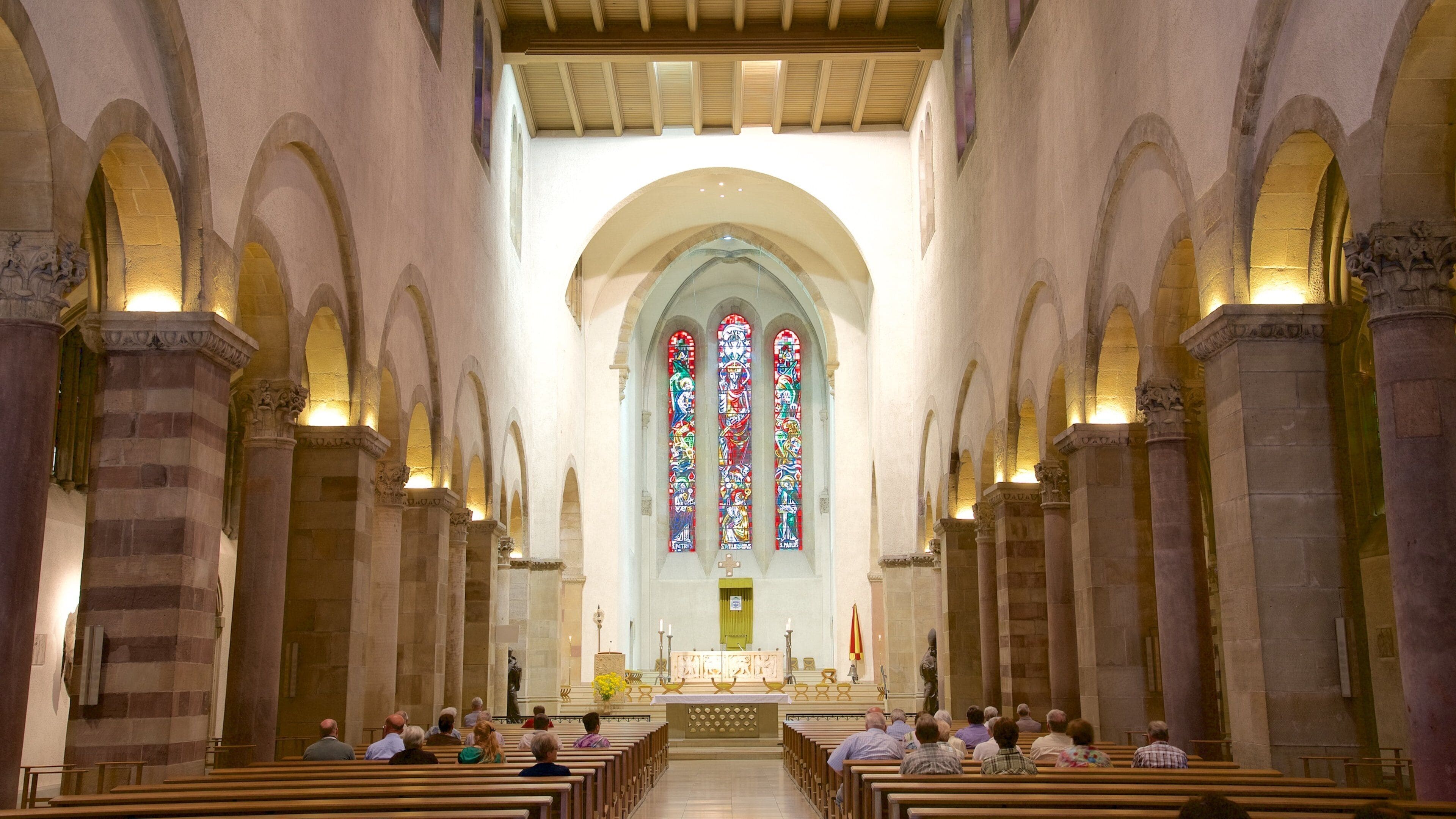 A church interior with arched ceilings, stained glass windows, and pews.
