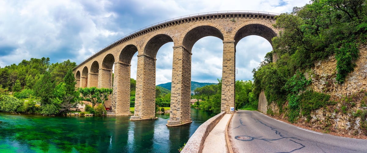 A stone bridge over a river with greenery on both sides.