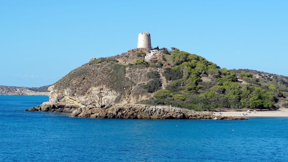 Une île côtière surmontée d’une tour imposante, entourée d’eaux d’un bleu limpide et d’un paysage rocheux.