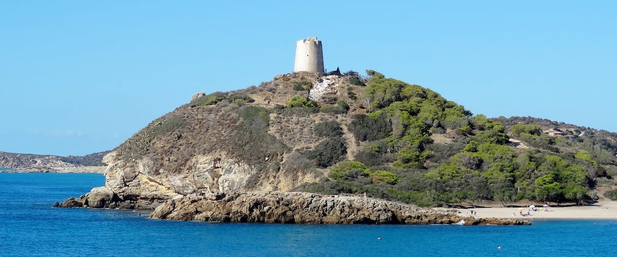 A coastal island with a prominent tower on top, surrounded by clear blue waters and rocky terrain.