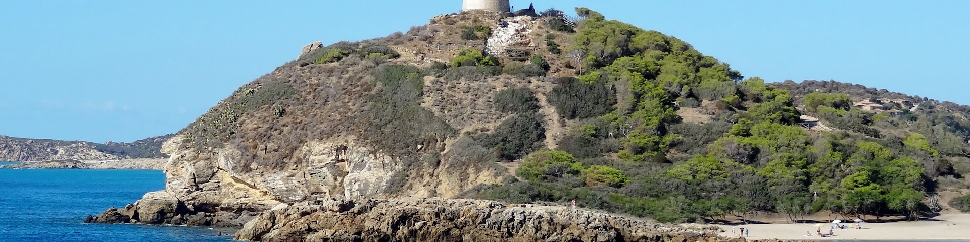 Una isla costera con una torre imponente en la cima, rodeada de aguas azules cristalinas y terreno rocoso.