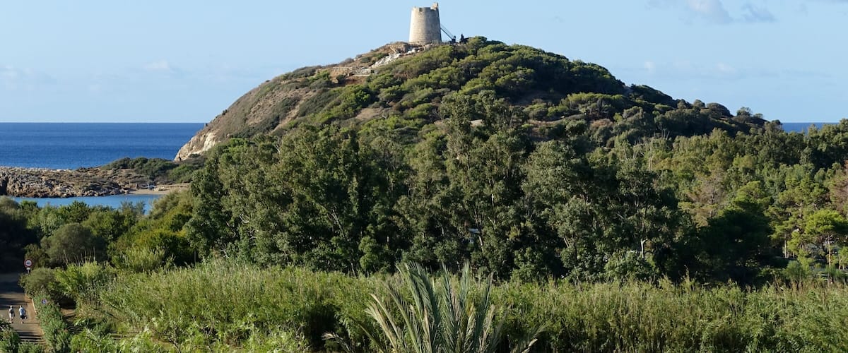 A hill with a tower on top, surrounded by greenery and a coastal view.