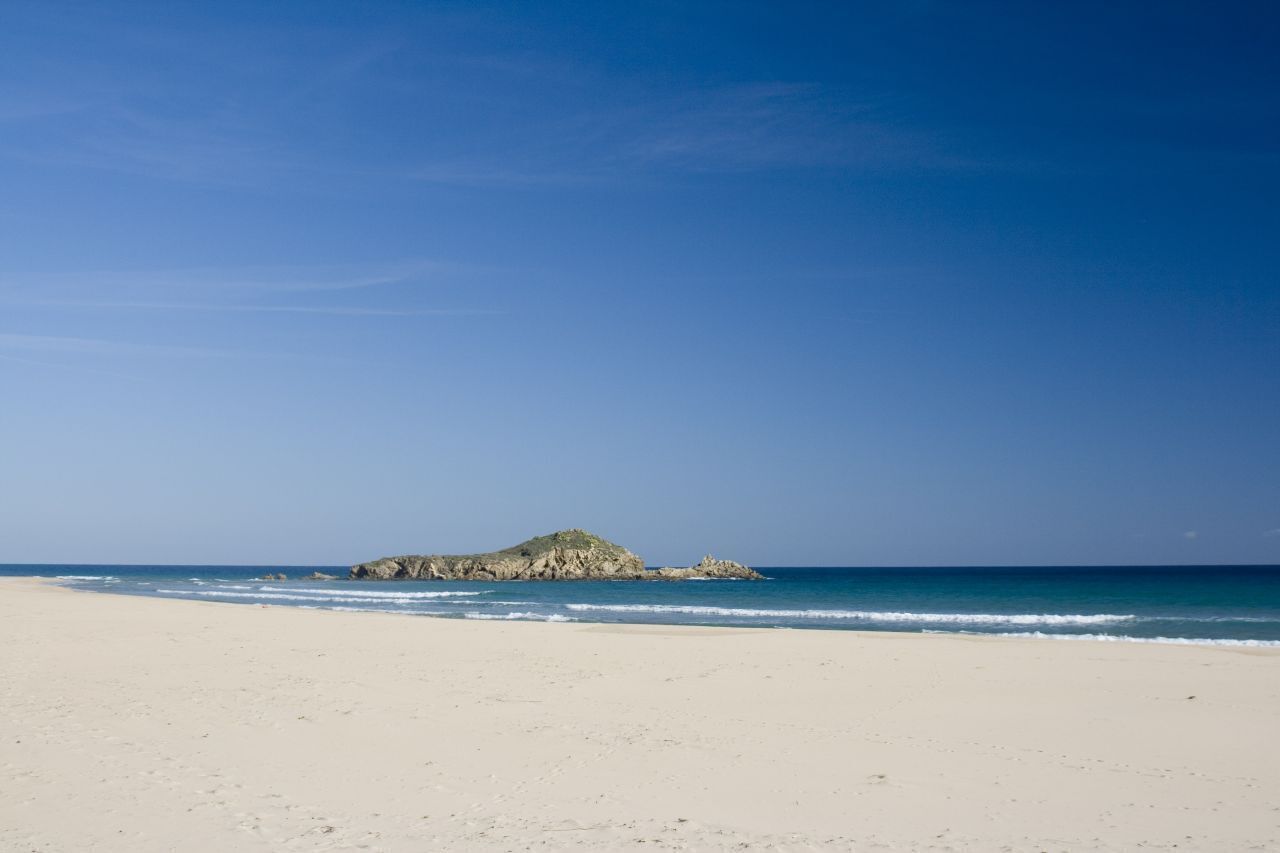 Una playa con un promontorio rocoso en la distancia.