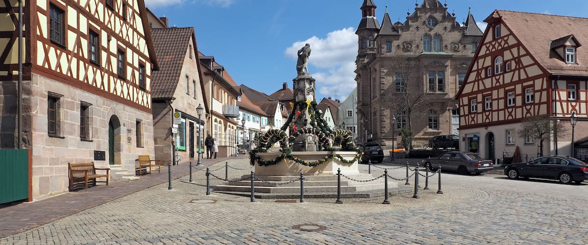 A cobblestone square with a fountain, traditional half-timbered buildings, and a church with a spire.