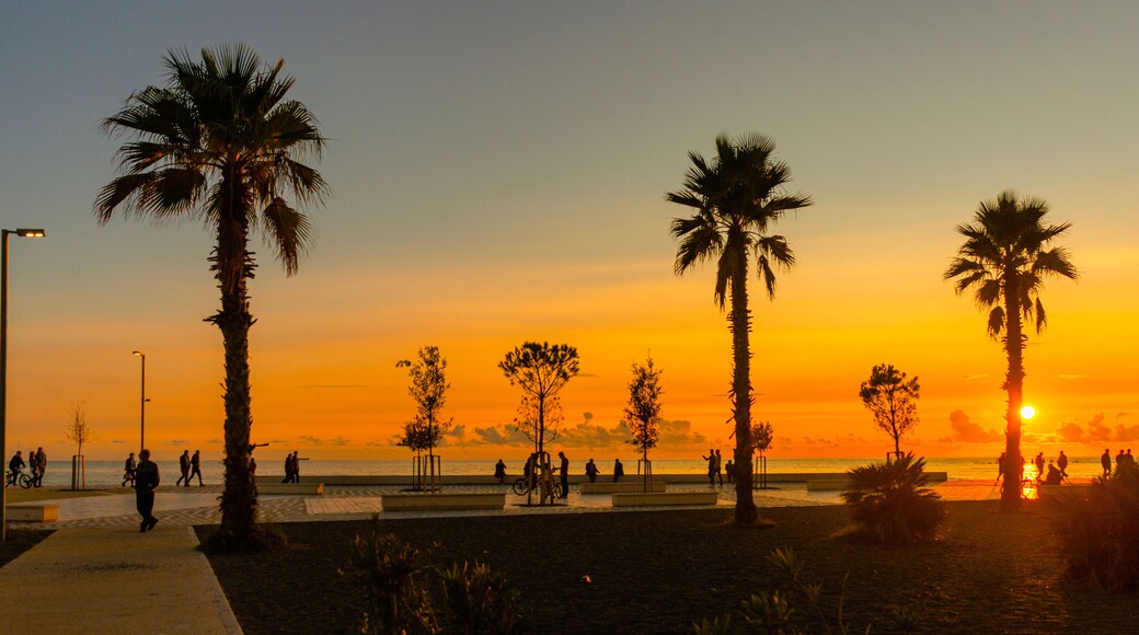 A sunset over a beach with palm trees and people walking.