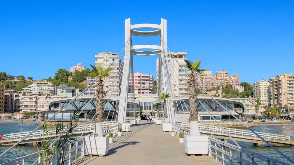 A modern bridge with a unique design, surrounded by coastal buildings and palm trees.
