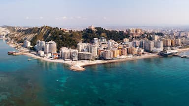 Paisagem costeira urbana com uma colina imponente, edifícios urbanos densos e um mar azul límpido.