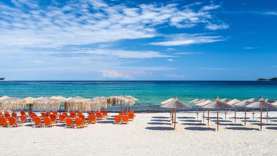 A beach with rows of orange chairs and straw umbrellas under a clear blue sky.