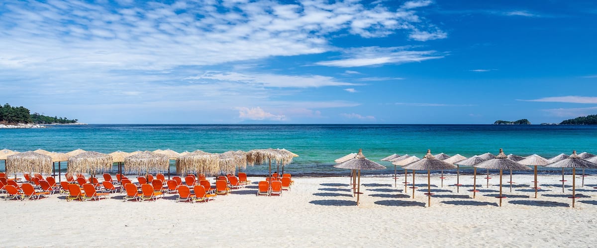 A beach with rows of orange chairs and straw umbrellas under a clear blue sky.