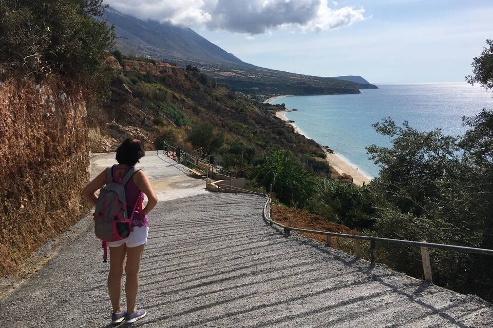 A person hiking up a stone staircase towards a beach with a mountain in the background.