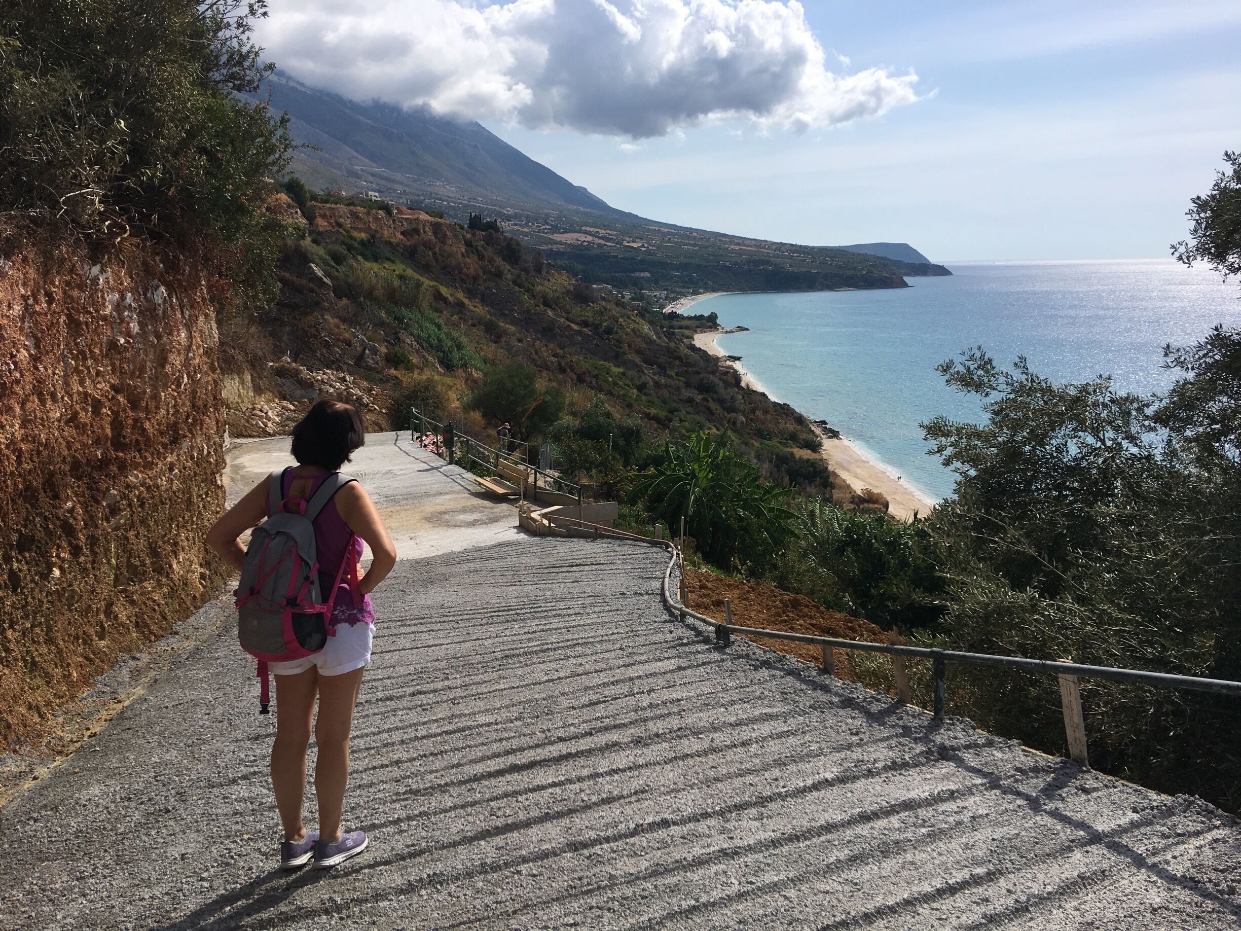A person hiking up a stone staircase towards a beach with a mountain in the background.