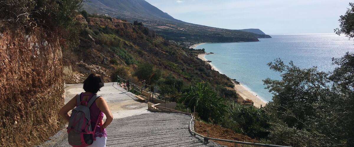 A person hiking up a stone staircase towards a beach with a mountain in the background.