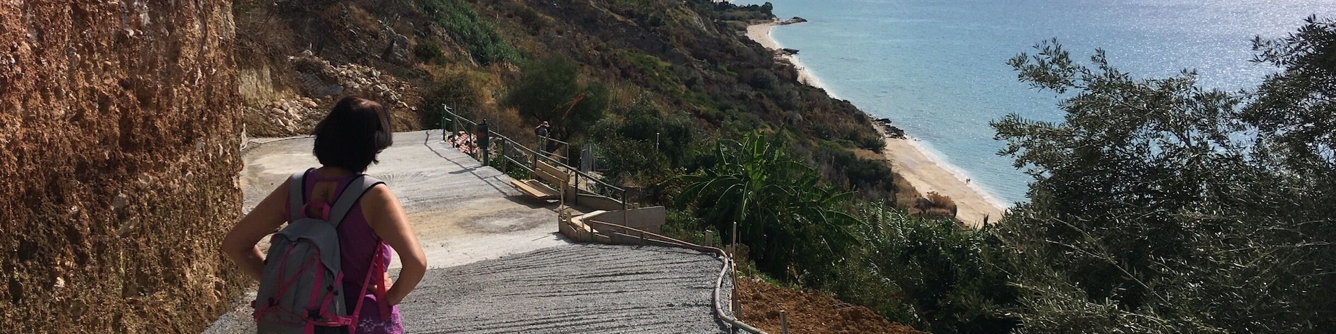 A person hiking up a stone staircase towards a beach with a mountain in the background.
