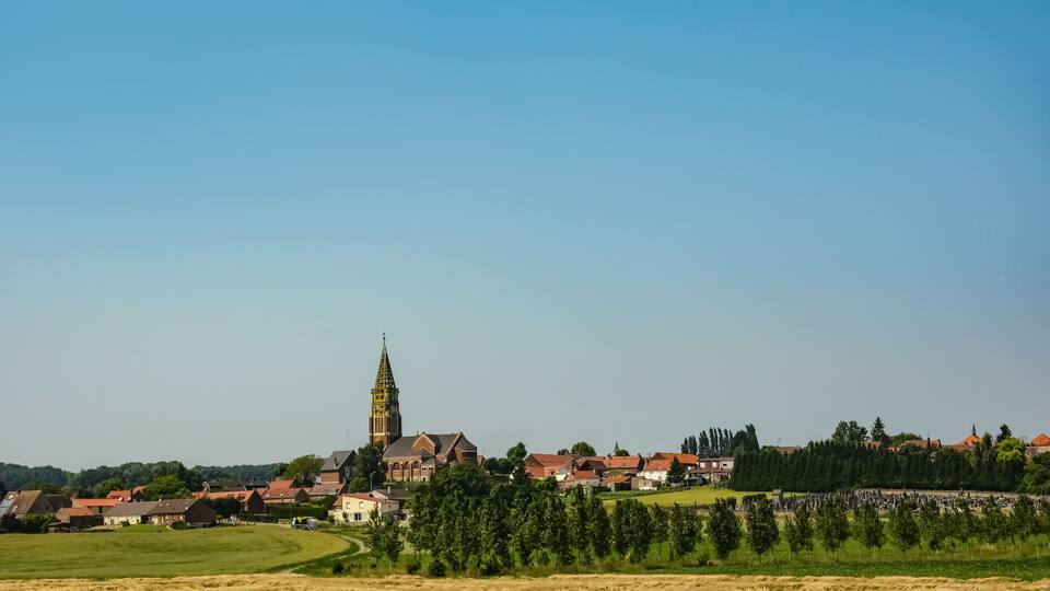 A town with a prominent church tower, surrounded by residential buildings and green fields.