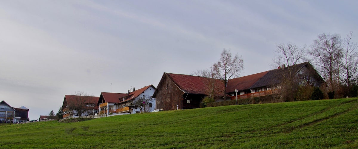 A rural landscape with houses on a hillside, a barn, and a clear sky.