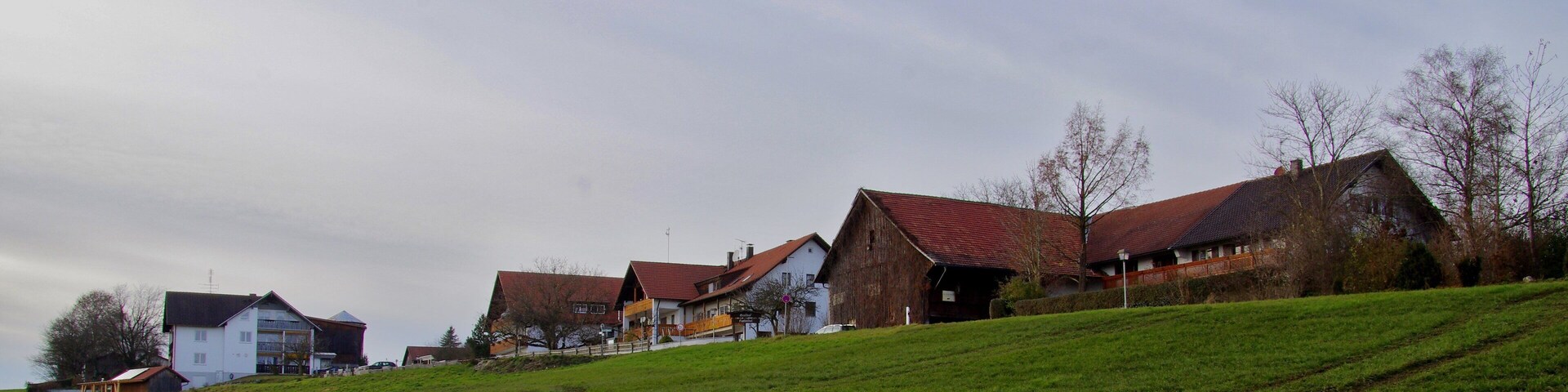 A rural landscape with houses on a hillside, a barn, and a clear sky.