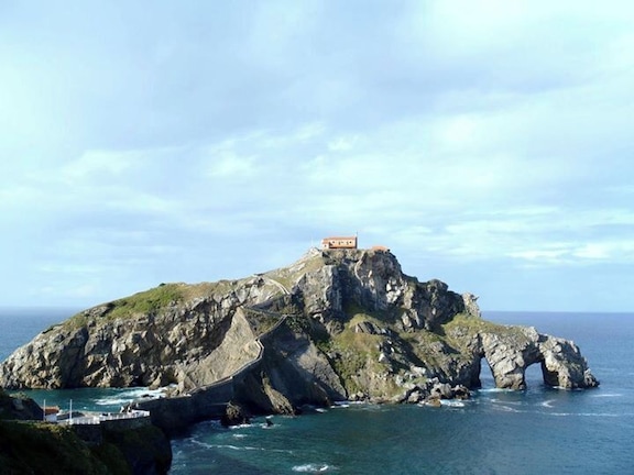 Une île rocheuse surmontée d’un bâtiment et reliée au continent par un pont.