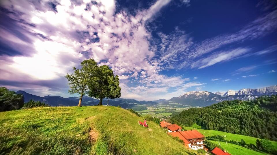 A mountainous landscape with a prominent tree, a red-roofed building, and a distant village.