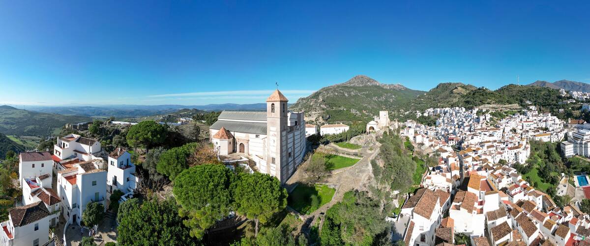 A town with white buildings, a church, and surrounding hills.