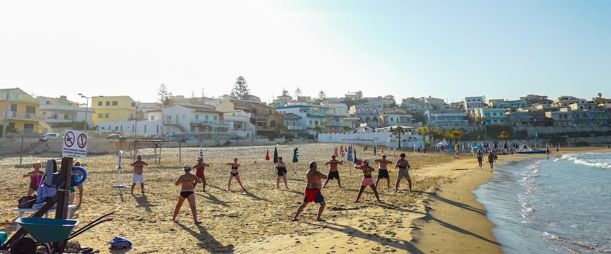 A beach with people sunbathing and swimming, surrounded by coastal buildings.