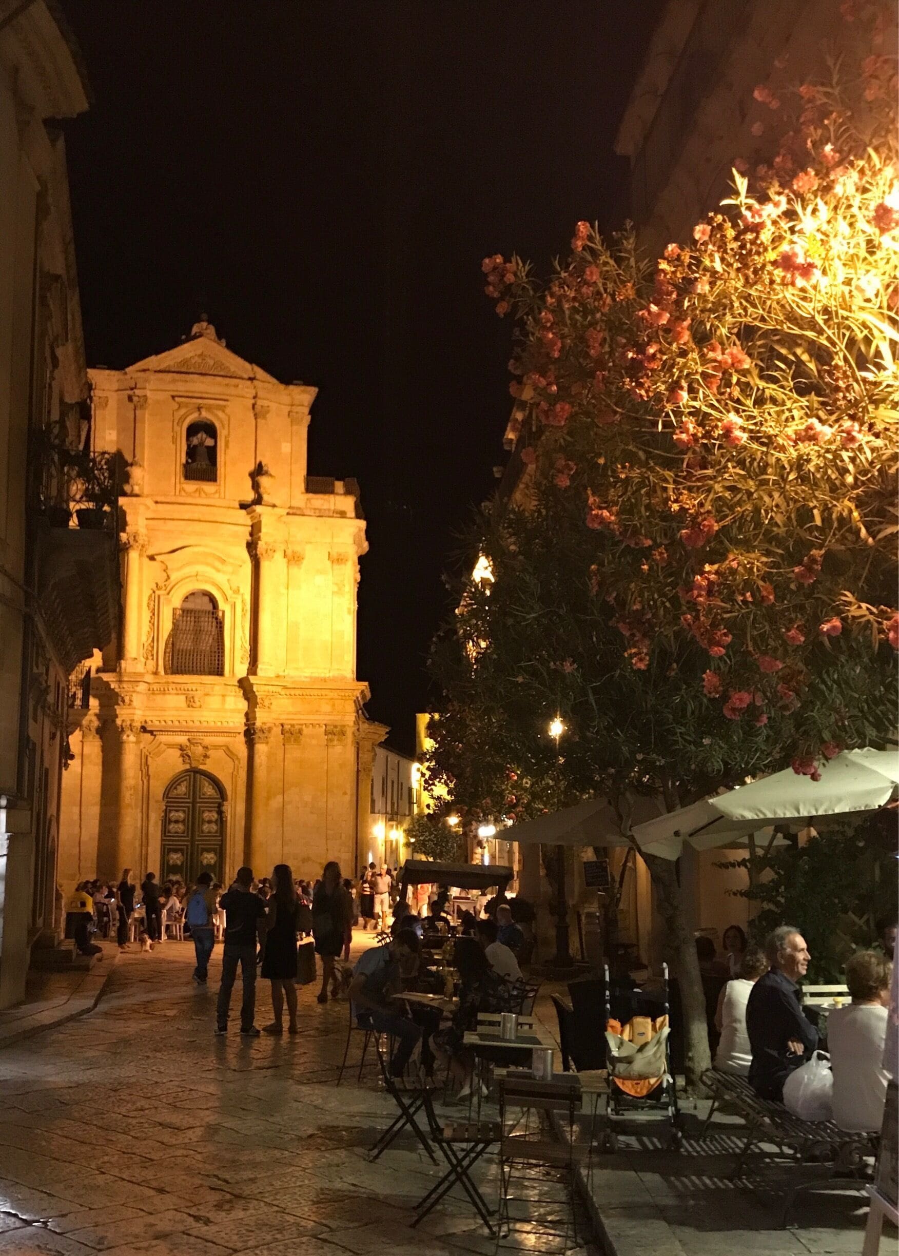 A historic building with a bell tower, surrounded by people and outdoor seating areas.