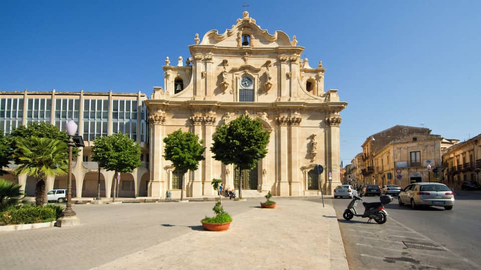 A historic building with ornate architecture, a clear blue sky, and a street with cars and pedestrians.